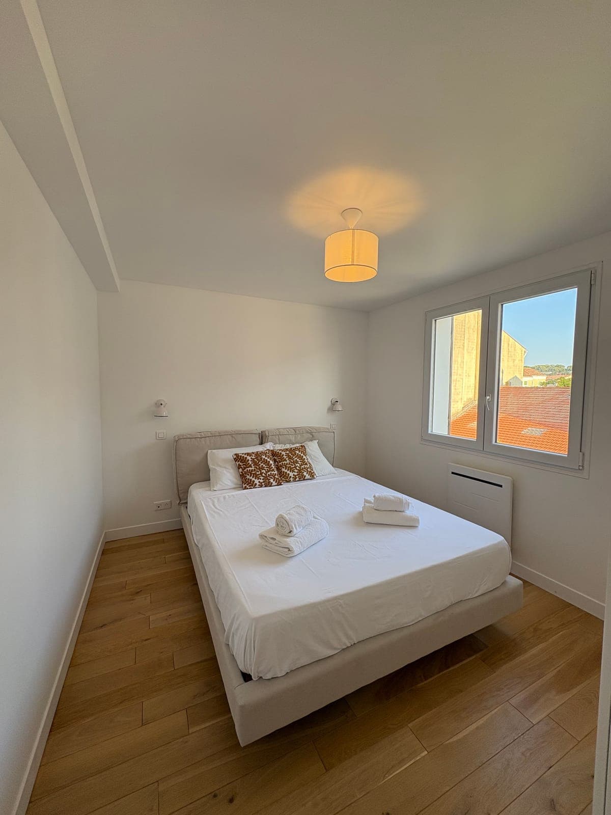 White linen bedroom, lifted by a single warm-toned cushion — Sanary-sur-Mer — two apartment furnishing project