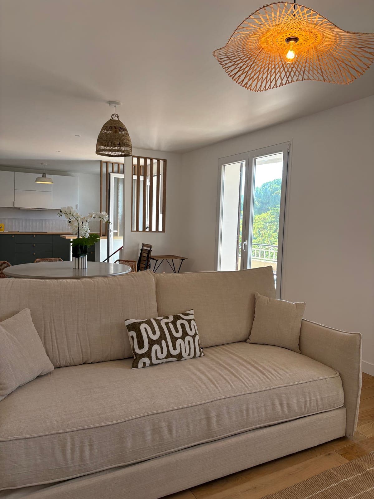 Neutral linen sofa with a patterned cushion under a woven rattan pendant light, Sanary-sur-Mer