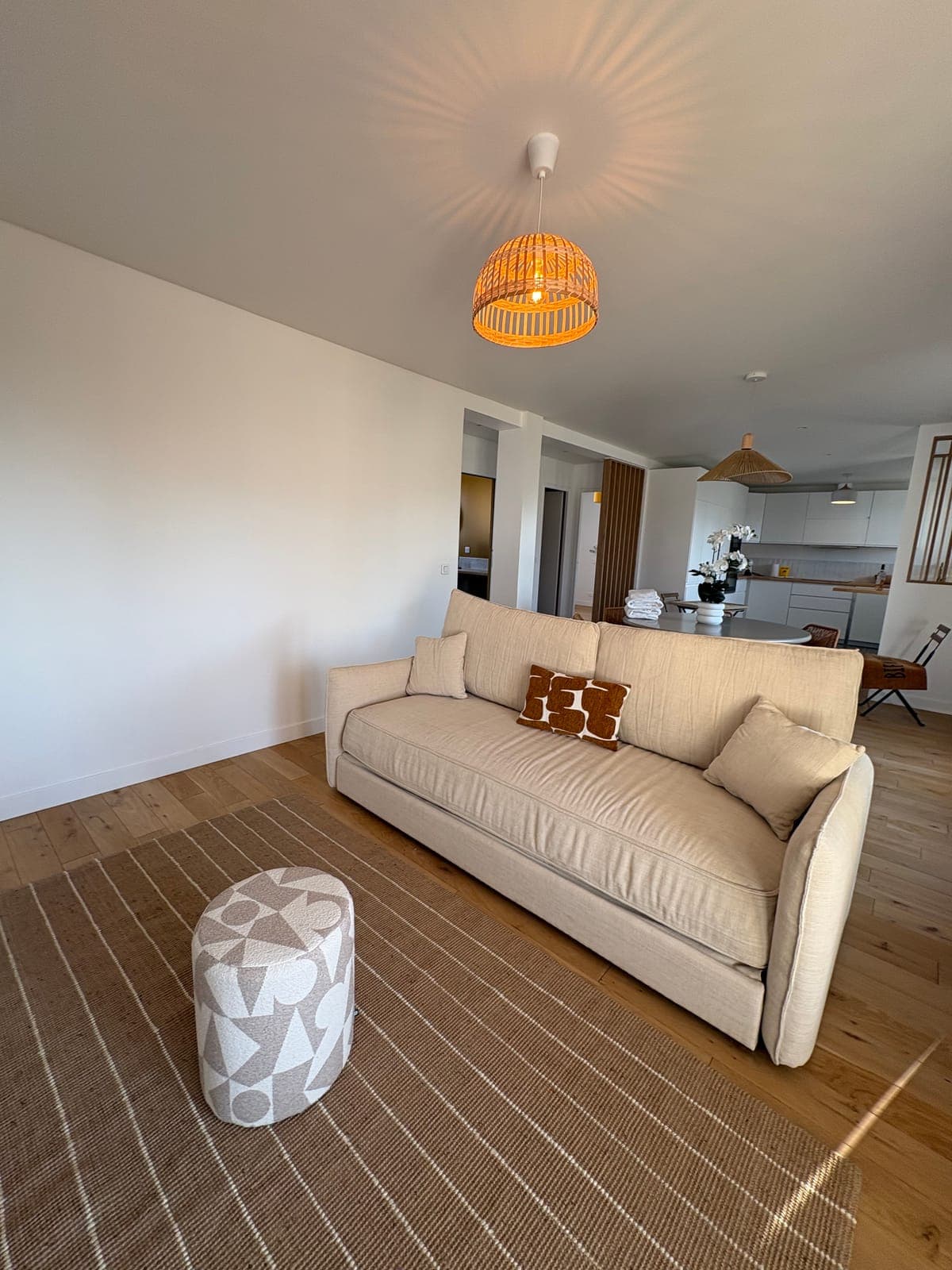 Linen sofa and jute rug, under a woven rattan pendant — Sanary-sur-Mer — two apartment furnishing project